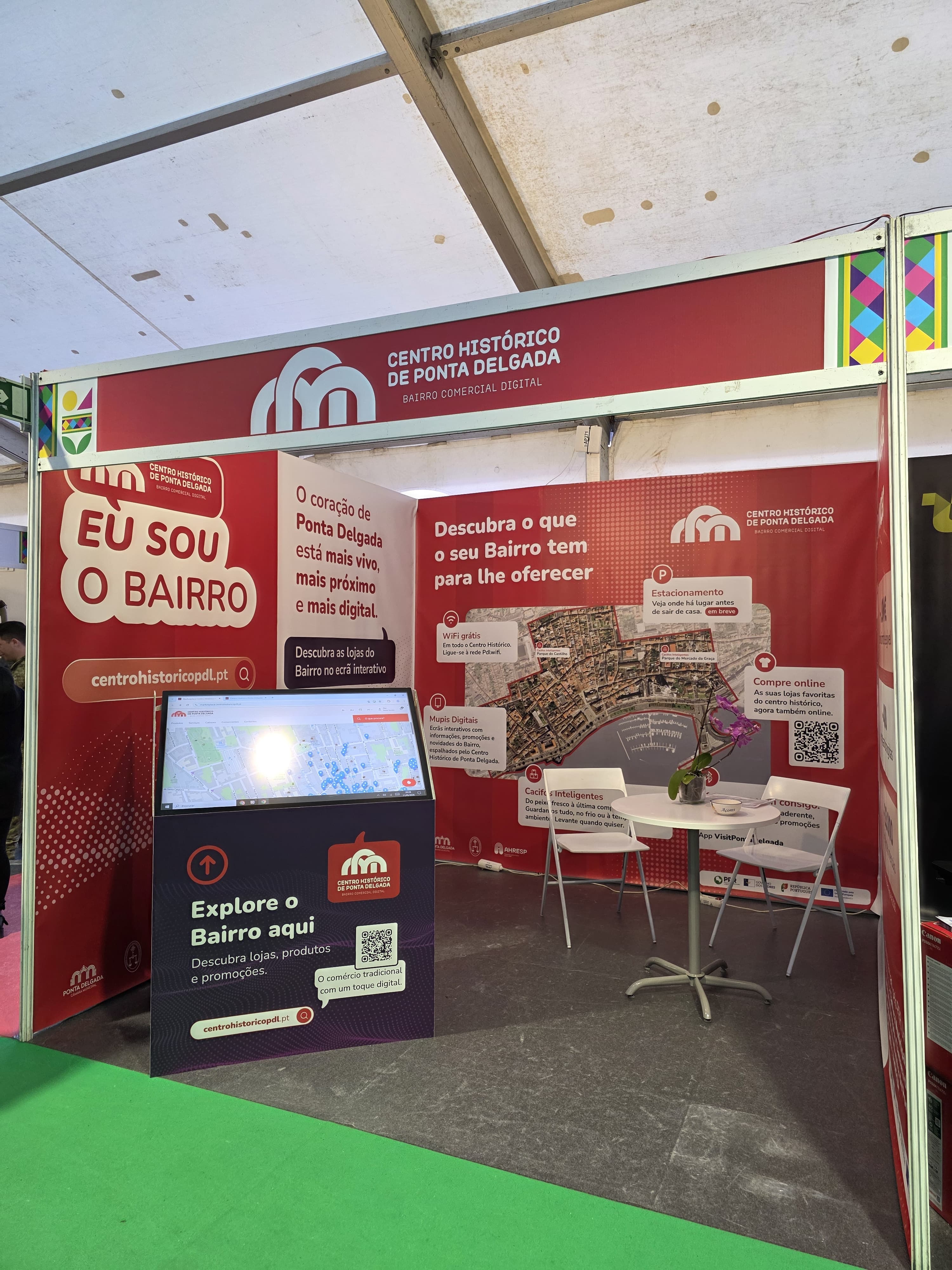 Detalhe do stand do Bairro Comercial Digital na FICSA 2026 com balcão de adesão para comerciantes